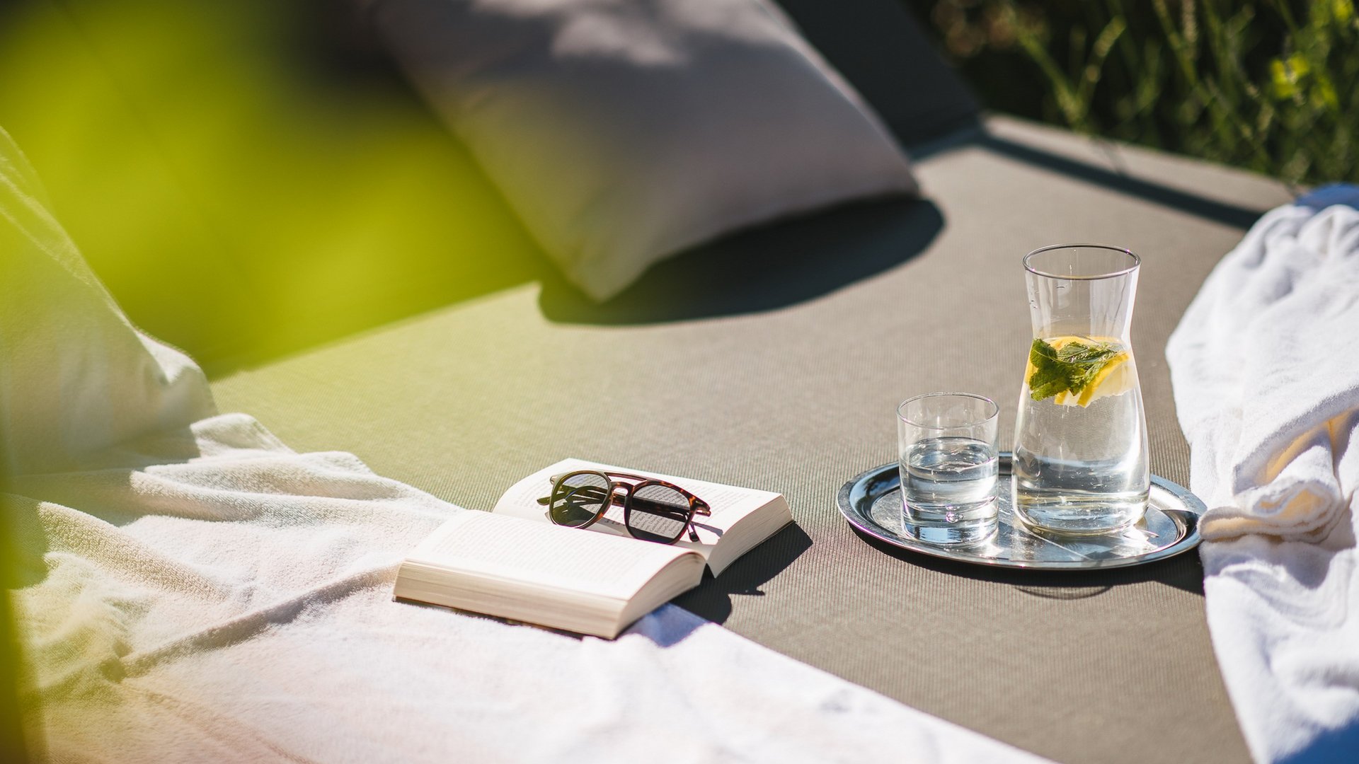 Sonnenliege mit Buch, Brille und Glas Karaffe mit Wasser und Zitrone